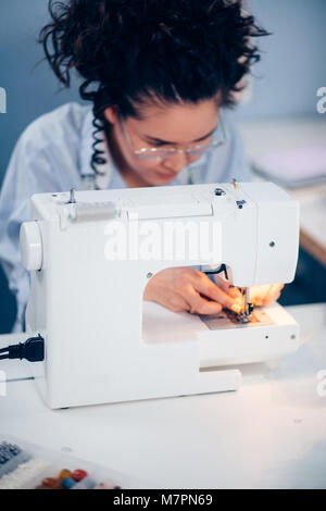 Giovane donna con scuri capelli ricci cucire sulla macchina da cucire in camera. small business. progettazione clothers Foto Stock