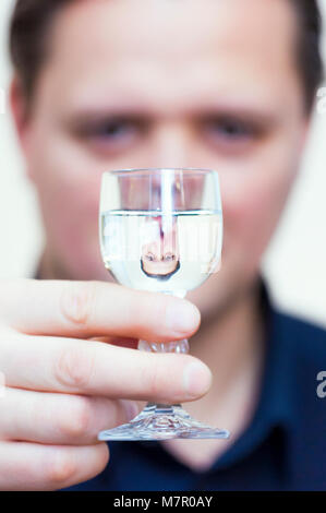 Ritratto di giovane etnia caucasica l uomo con la maglietta blu e il suo capovolto riflessione nella vodka shot in vetro. Foto Stock