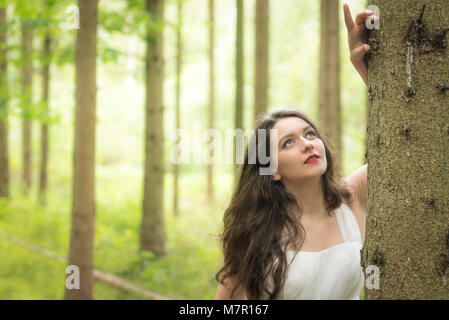 Ritratto di una giovane donna bruna in un paesaggio di primavera in una foresta appoggiato su una struttura ad albero Foto Stock