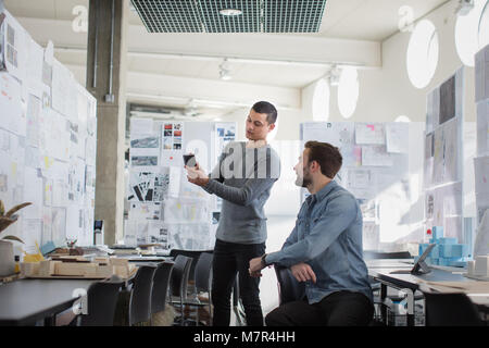 I progettisti guardando smartphone in area di lavoro creativo Foto Stock