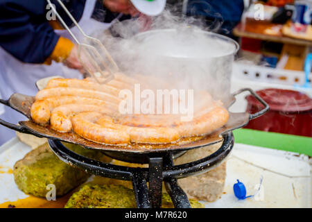 Mano con l'aiuto delle pinze in metallo gira la simmering salsicce su un nero barbecue grill. Foto Stock