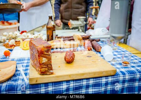 Headcheese e salsiccia affumicata su un tagliere di legno a cucina esterna, persone in background sono la preparazione di carne per salsiccia fatti a mano. Foto Stock