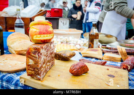 Headcheese e salsiccia affumicata su un tagliere di legno a cucina esterna, persone in background sono la preparazione di carne per salsiccia fatti a mano. Foto Stock
