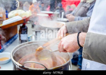 Mano con l'aiuto delle pinze in metallo gira la simmering salsicce su un nero barbecue grill. Foto Stock