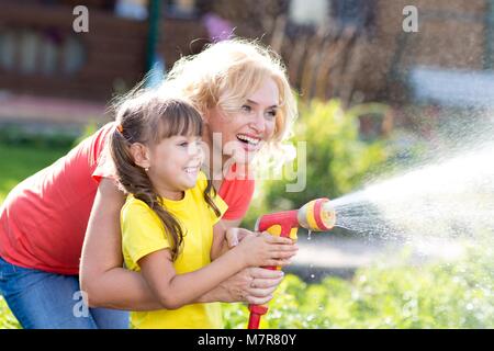 Pretty Woman e sua figlia di innaffiamento con tubo flessibile in giardino Foto Stock