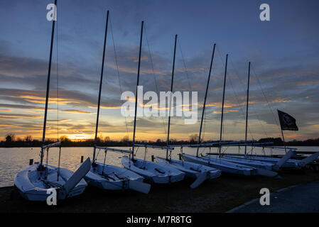 Fila di sette dingeys vela sul bordo di un lago al tramonto Foto Stock