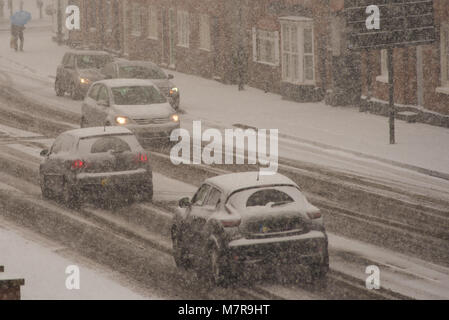 Caos del traffico nel Regno Unito con le automobili che viaggiano lungo la coperta di neve strada durante condizioni di blizzard Foto Stock
