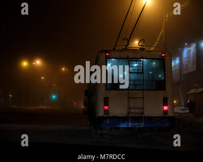 White filobus la guida pericolosamente nella nebbia all'inverno nevoso notte Foto Stock