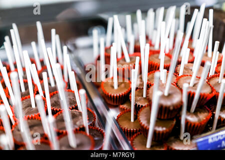 Primo piano del latte brown torta al cioccolato fondente pops lollipos su bastoni in rosso muffin liner di carta sul display nel negozio di caramelle shop tazze di tartufi Foto Stock