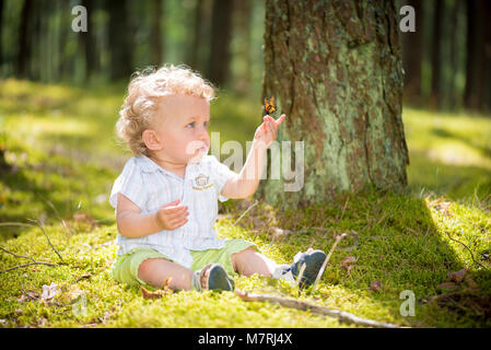 1 anno di età baby esaminando farfalla posata sulla sua mano Foto Stock