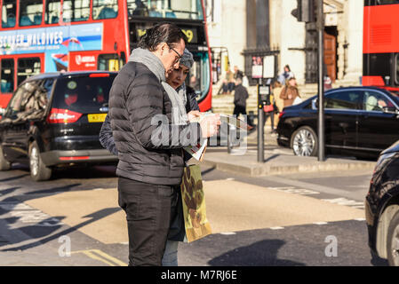 I turisti alla ricerca di mappa a Londra con il bus rosso e del traffico. Turismo. Maschio e femmina giovane. Persone. La Gran Bretagna. British. Direzioni Foto Stock