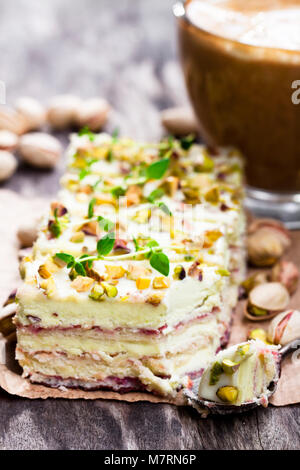 Fette di torta a strati con pistacchio e una tazza di caffè con marshmallow Foto Stock