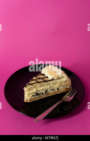 Fetta di torta di strato con crema e scaglie di cioccolato sulla piastra nera con forcella - su hot sfondo rosa - Spazio di copia Foto Stock