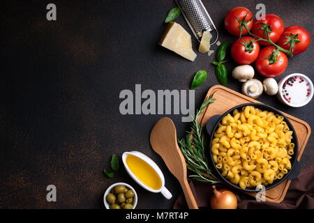 La pasta e gli ingredienti per cucinare su sfondo scuro, vista dall'alto. Il cibo italiano concetto. La pasta, i pomodori, il basilico, spezie e verdure. Spazio di copia Foto Stock
