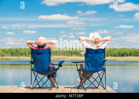 L uomo e la donna rilassarsi su un molo vicino a un lago seduti su sedie Foto Stock