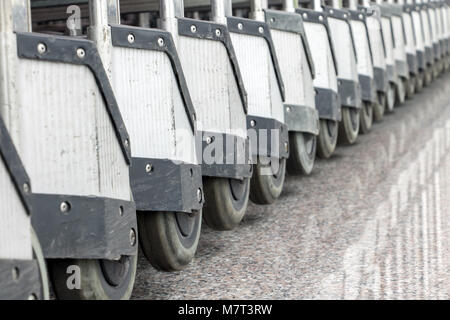 Una fila diagonale di carrelli nella hall, vista da vicino. Le ruote dei carrelli al terminal dell'aeroporto. Foto Stock