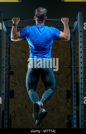 L'atleta tira se stesso sulla barra nella palestra vista dal retro Foto Stock