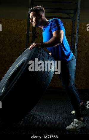 Forte giovane atleta con una grande ruota pesante in palestra Foto Stock