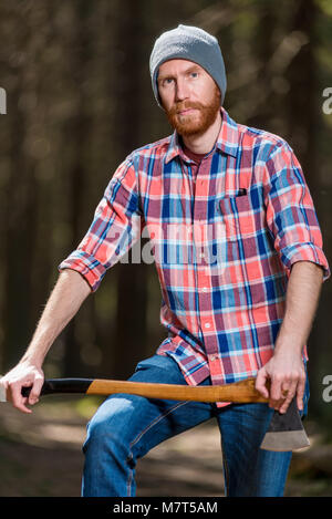 Ritratto di un uomo in un plaid shirt con un'ascia nella foresta Foto Stock