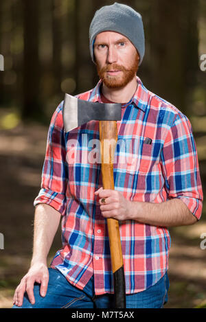 Un guardaboschi con una barba rossa in posa di una foresta con un'ascia Foto Stock