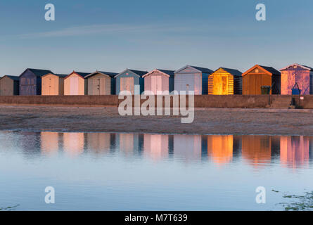 Luce dorata al tramonto con le colorate cabine in legno si riflette nell'acqua a Brightlingsea, Essex. Foto Stock