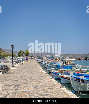 Una passeggiata in Elounda, Creta, si estende nella distanza. Una miriade di piccole barche da pesca sono ormeggiate su un lato. Foto Stock