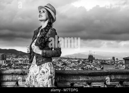 Serata perfetta con vista mozzafiato. sorridente giovane viaggiatore donna in abiti lunghi e cappello di paglia nella parte anteriore del paesaggio urbano di Barcellona, Spagna cercando in Foto Stock