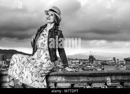 Serata perfetta con vista mozzafiato. Felice donna moderna in abiti lunghi e cappello di paglia nella parte anteriore del panorama della città di Barcellona, Spagna cercando la Foto Stock