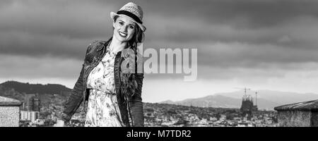 Serata perfetta con vista mozzafiato. Felice viaggiatore eleganti donna in abiti lunghi e cappello di paglia contro il paesaggio urbano di Barcellona, Spagna Foto Stock