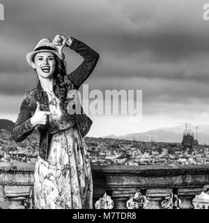 Serata perfetta con vista mozzafiato. Sorridendo donna moderna in abiti lunghi e cappello di paglia nella parte anteriore del paesaggio urbano di Barcellona, Spagna con le mani il framing Foto Stock