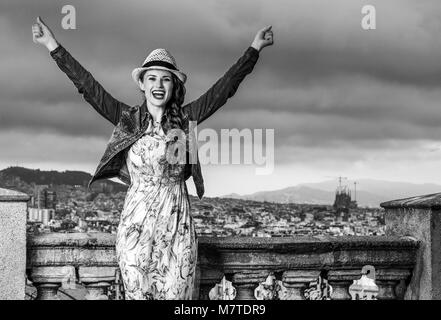 Serata perfetta con vista mozzafiato. Felice elegante donna in abiti lunghi e cappello di paglia nella parte anteriore del paesaggio urbano di Barcellona, Spagna gioia Foto Stock