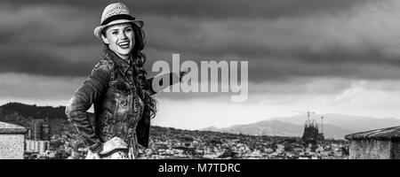 Serata perfetta con vista mozzafiato. Sorridendo turistico alla moda donna in abiti lunghi e cappello di paglia nella parte anteriore del paesaggio urbano di Barcellona, Spagna puntando al Foto Stock