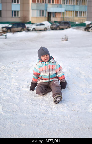 Funny capretto piccolo ragazzo in abiti colorati giocare all'aperto in inverno nelle fredde giornate innevate. Bambino felice divertirsi e giocare con la neve Foto Stock