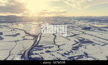 Vista aerea del fiume che scorre attraverso la coperta di neve la campagna al tramonto. Foto Stock