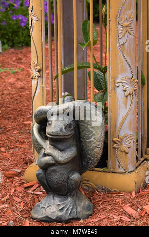 Close-up di scultura di rana accanto al pilastro su golden ferro battuto metal gate pergolato in giardino nel cortile in estate Foto Stock