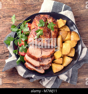 Arrosto di maiale con erbe e verdure su tavola in legno rustico. Foto Stock