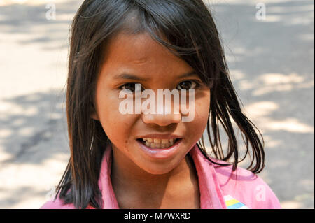 Ritratto di un sorridente, mendicante ragazza in attesa per i turisti alla banchina, Angkor Wat, Cambogia. Chiusura del bel bambino con grandi occhi marroni, in rosa Foto Stock