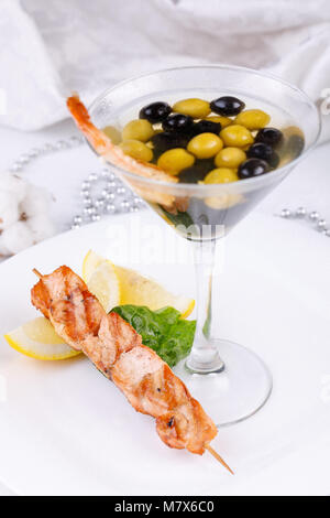 Snack freddi da gamberi e pesce shish kebab con originale che serve di olive in un elegante vetro. Close-up. Foto Stock