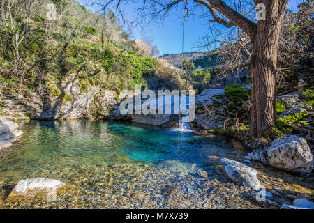 Vista della piccola cascata sul fiume attuale alla luce del sole. Stagno con il verde e l'acqua chiara. Foto Stock