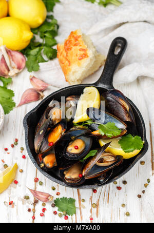 Deliziosa cozze al vino bianco con limone, aglio, erbe aromatiche e spezie in una padella in ghisa . Baguette, il coriandolo e il pepe. Frutti di mare. Le vongole in essa Foto Stock