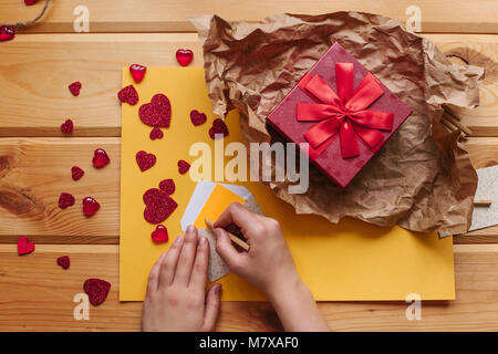 La ragazza scrive una lettera e lo mette in una busta. Il prossimo è un dono fatti a mano in una bella scatola rossa fasciata con nastro. La creazione. Celebrando la ev Foto Stock