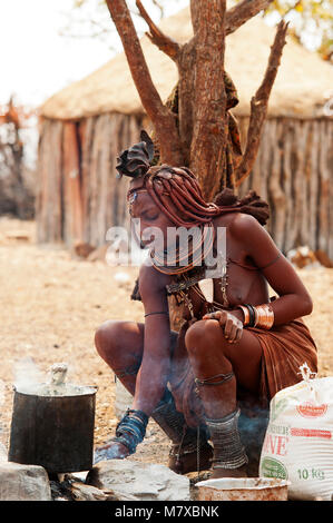 Donna Himba la cottura di alimenti a base di farina di granturco nel suo villaggio vicino a Epupa Falls. Himbas normalmente si trovano nei pressi delle cascate e villaggi vicini, Namibia Foto Stock