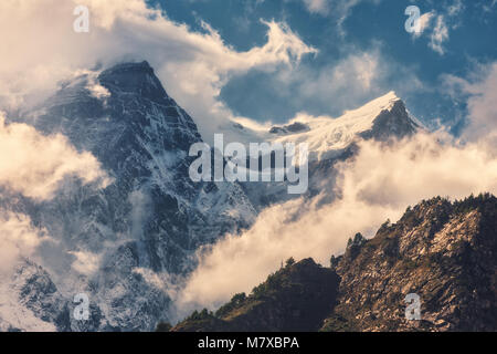 Alte montagne con vette innevate in nuvole a bright sunny serata in Nepal. Paesaggio colorato con splendide rocce e drammatico cielo nuvoloso al tramonto. Foto Stock