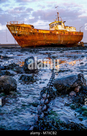 Vecchio arrugginito peschereccio fregata a bassa marea su una banca di fango le barche grandi a lunga catena di ancoraggio va dal centro al primo piano la barca in backgro Foto Stock