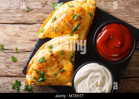 Il cibo italiano: pizza calzone con carne e verdure e formaggio vicino sul tavolo. parte superiore orizzontale vista da sopra Foto Stock