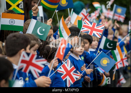 Bambini bandiere d'onda come la duchessa di Cornovaglia arriva a frequentare un Commonwealth Big Pranzo con gli allievi della scuola primaria, al granaio Croft scuola primaria, Londra. Foto Stock