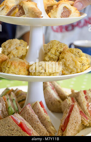 Tè inglese pomeridiano costituito da panini e focaccine di formaggio e salsicce rotola su una torta a più livelli di stand Foto Stock