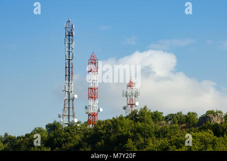 Tre le telecomunicazioni (GSM) torri con antenne TV ,parabole satellitari e ripetitori in cima ad una collina su un cielo blu ed una nube su sfondo Foto Stock