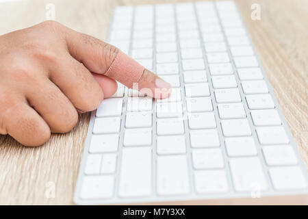 Vicino la mano con il pregiudizio sul dito bianco utilizzando la tastiera del computer su sfondo di legno Foto Stock