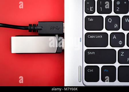 Un flash drive e un filo da un disco rigido esterno collegato a un computer portatile su uno sfondo di colore rosso. Il concetto di supporto portatile per la memorizzazione dati Foto Stock